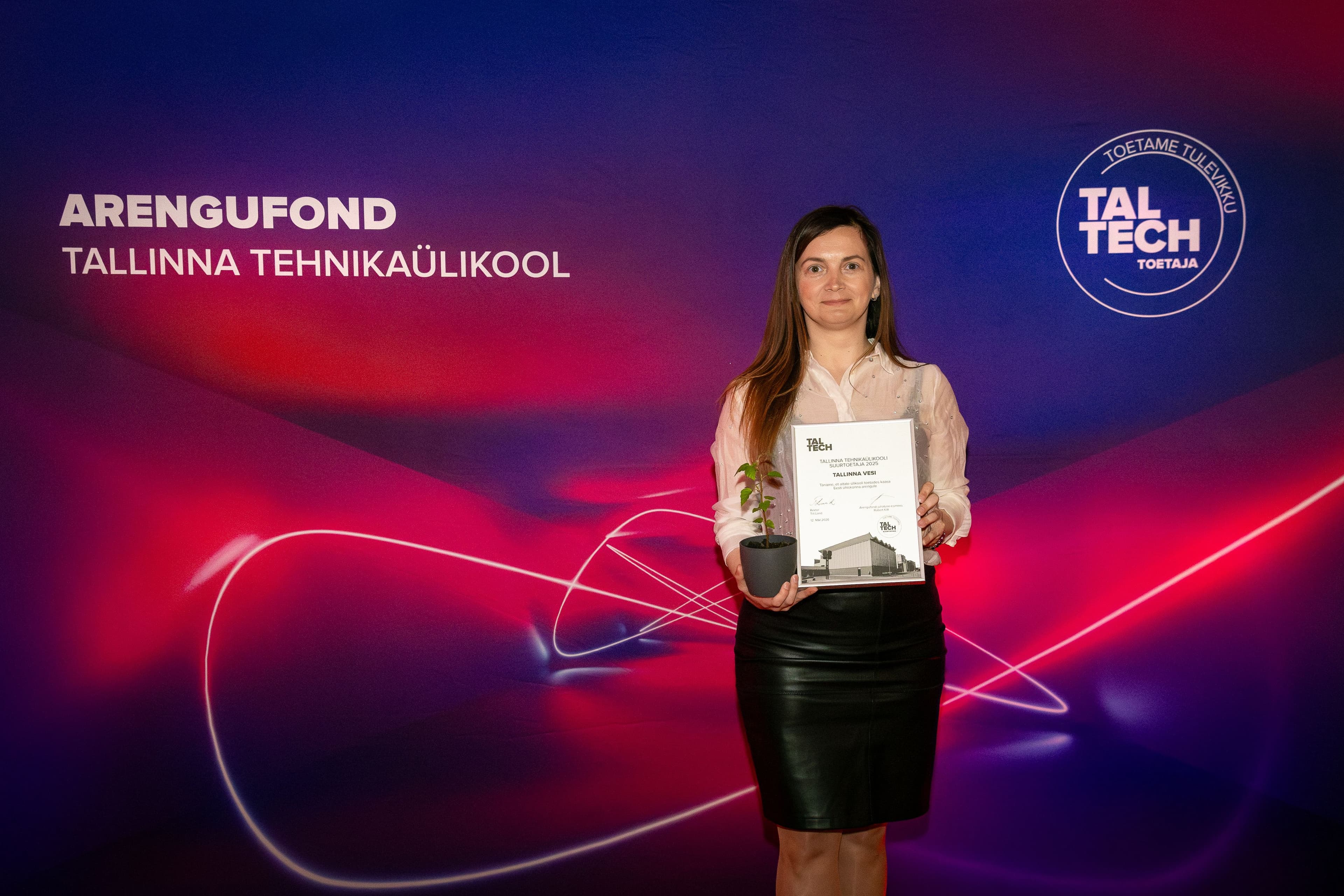 Woman holds certificate and plant award at a vibrant TalTech recognition event.