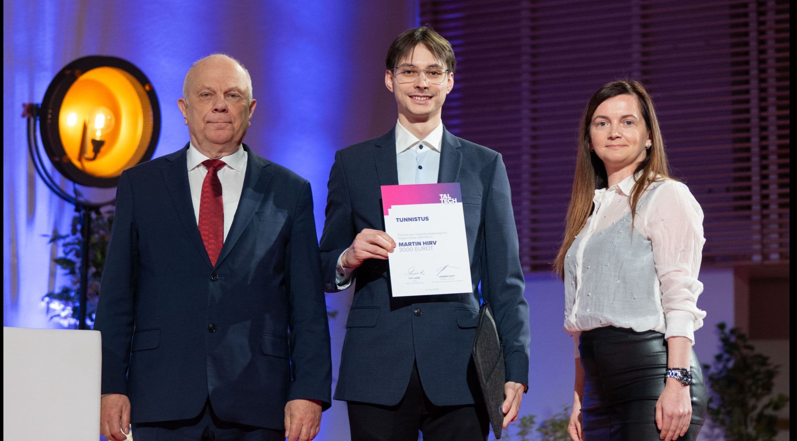 Young man receives a certificate from two adults on a stage at an award ceremony.