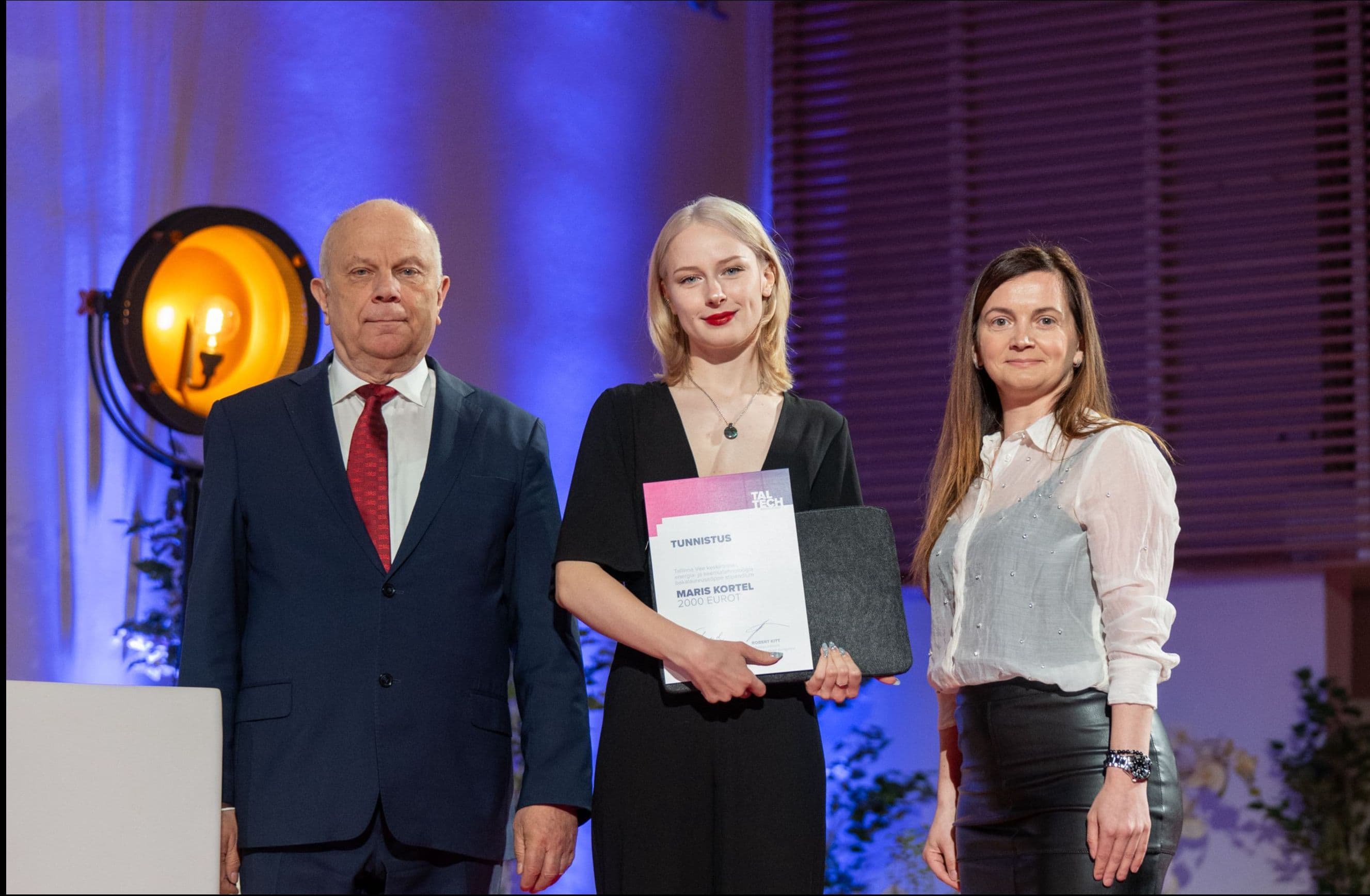 A woman receives an award certificate from a man and another woman on stage.