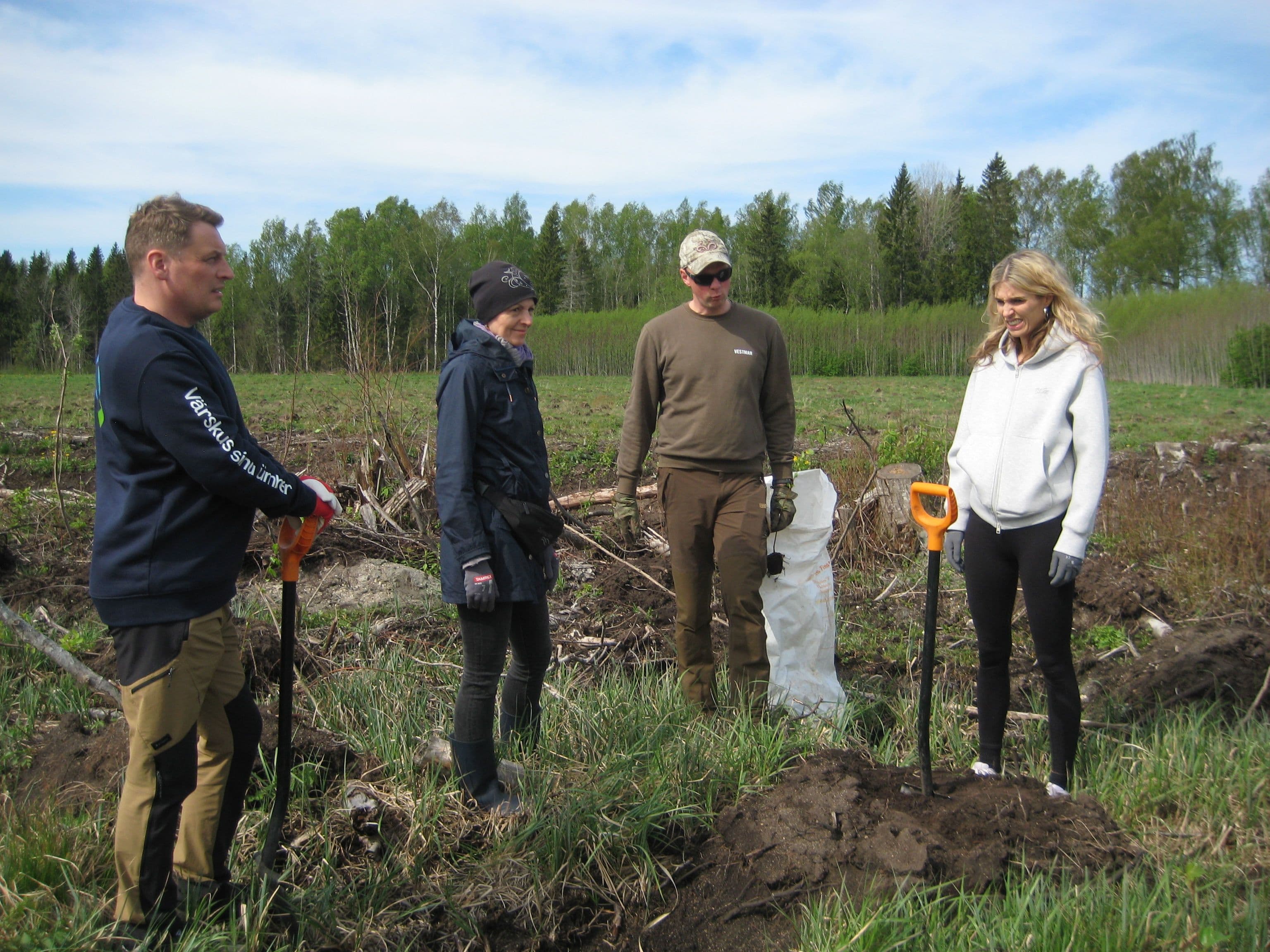 Four people are engaged in outdoor planting or cleanup, with shovels in a cleared area.