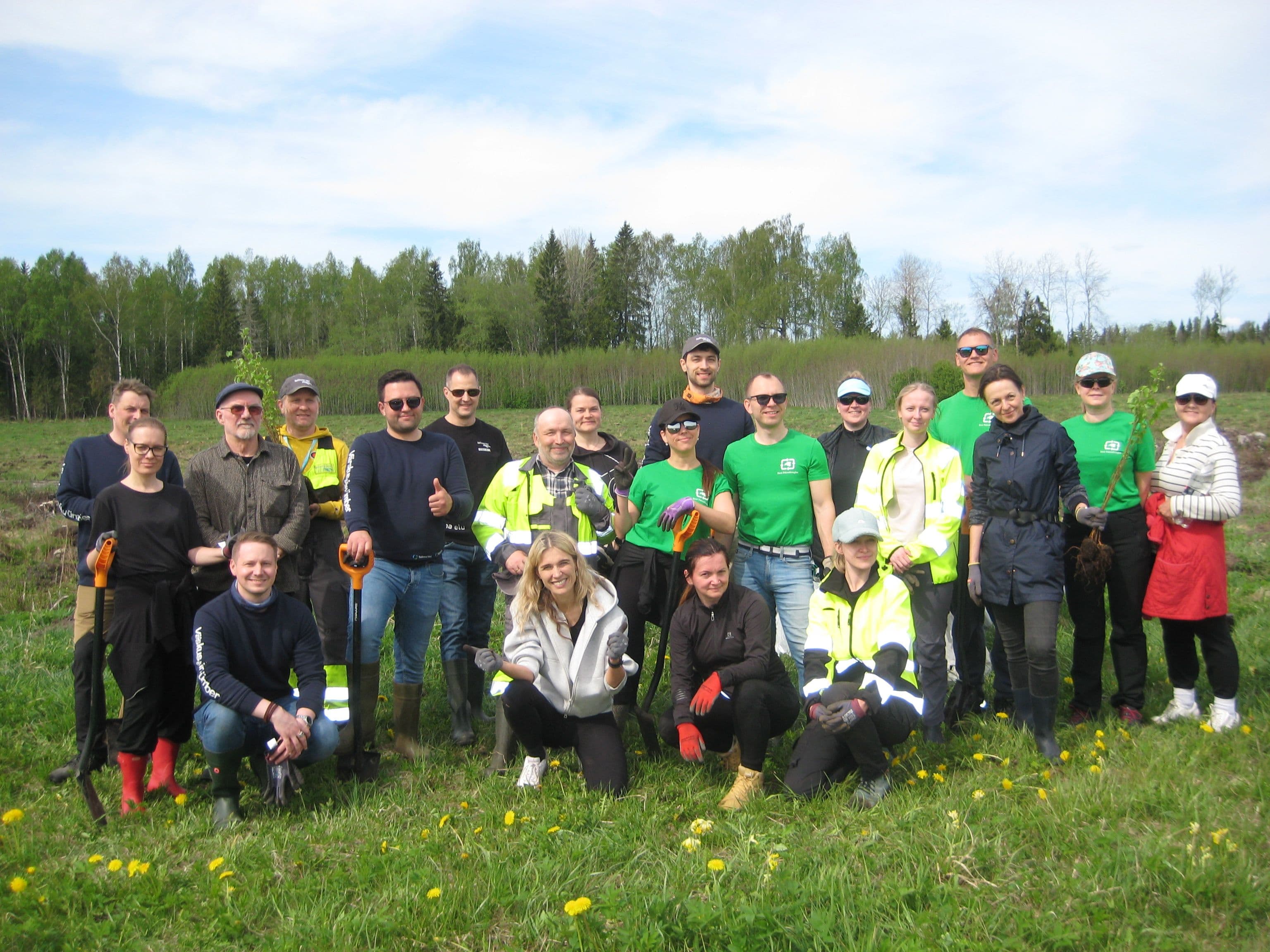 A diverse group of people gathers outdoors in a field with trees in the background.