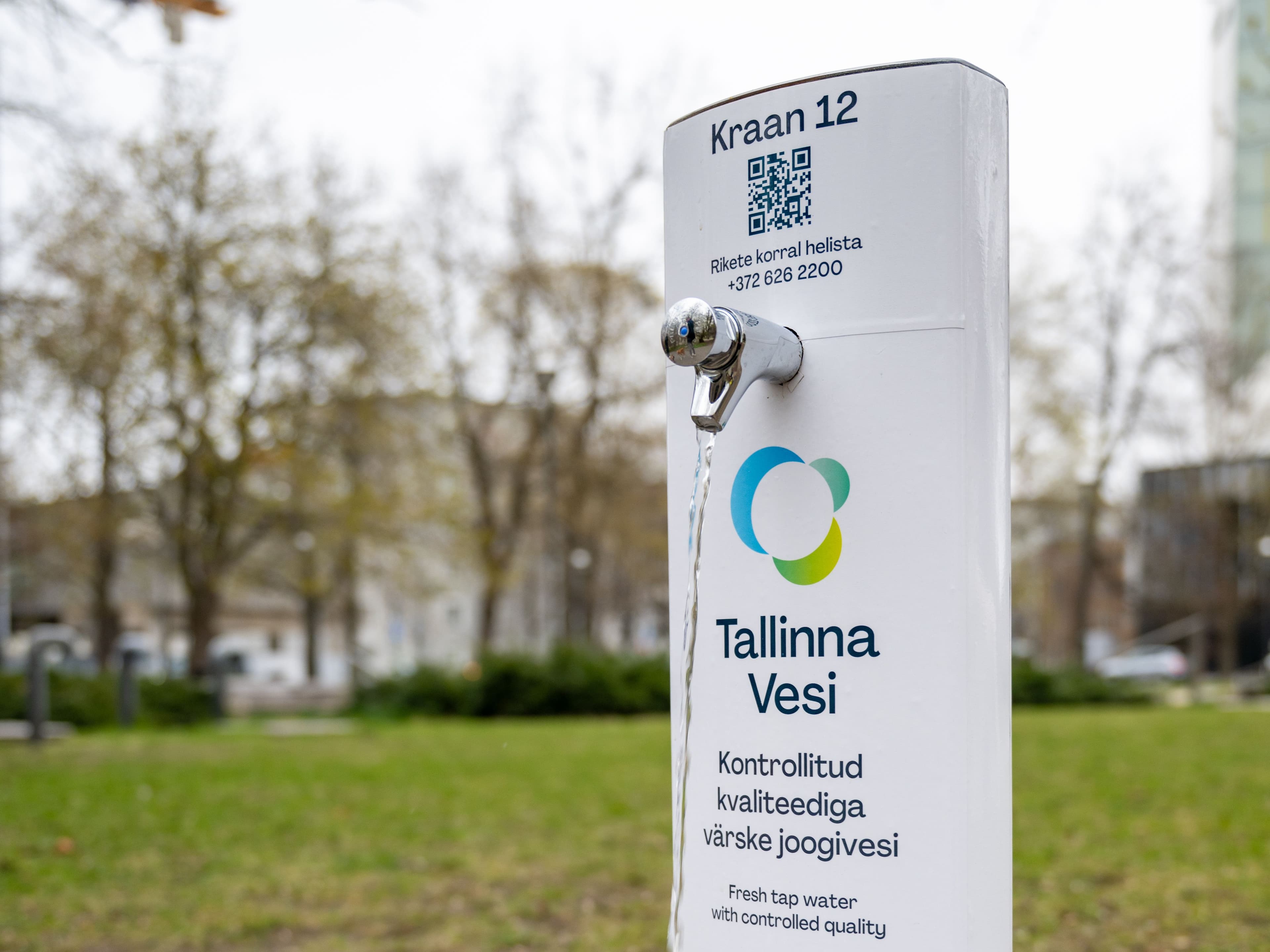 White public water dispenser with 'Tallinna Vesi' logo and faucet outdoors.
