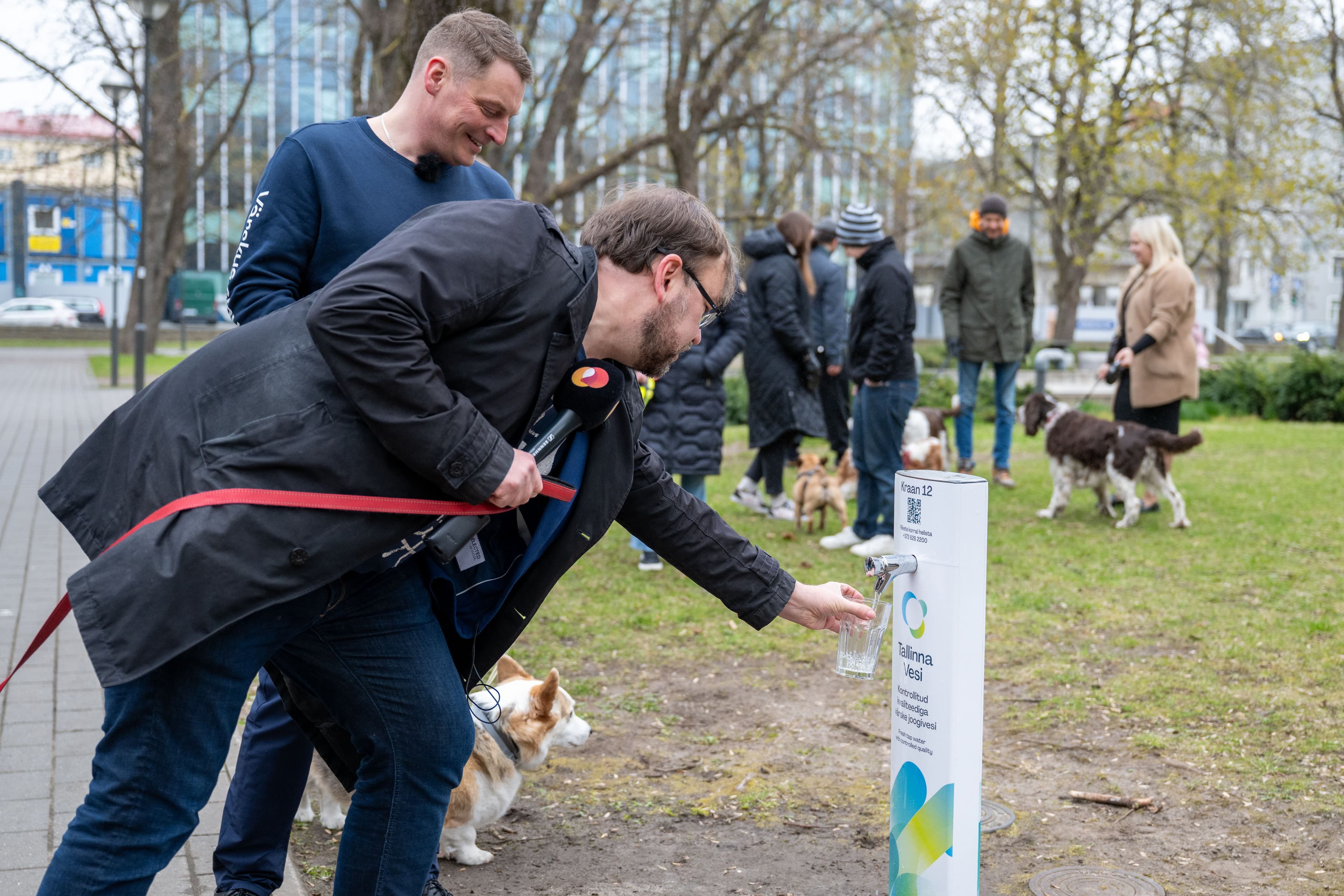 A man with glasses pours water into a public dog watering station in a park.