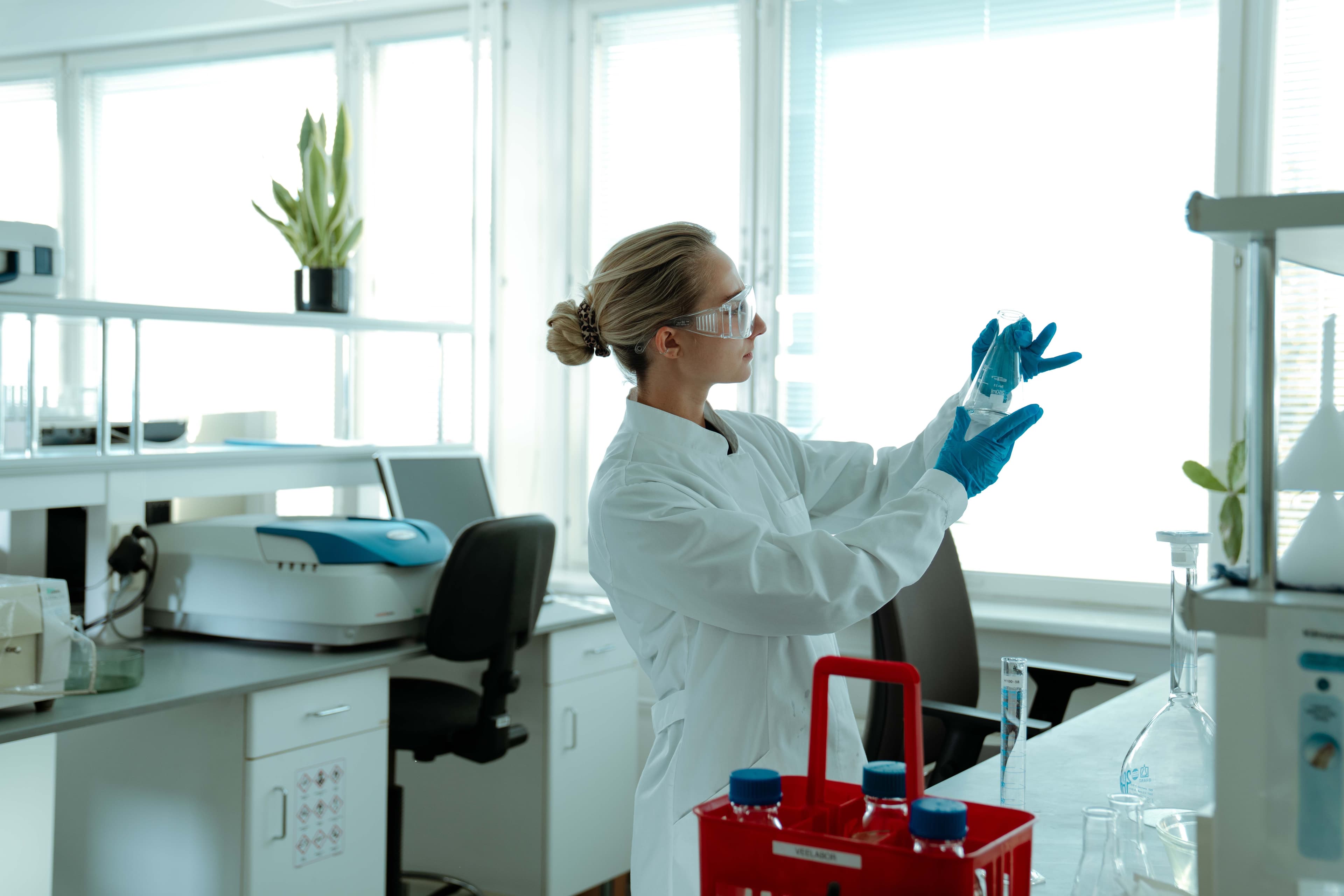 Naine teadlane valges kitlis ja sinistes kinnastes uurib proovi steriilses laboris