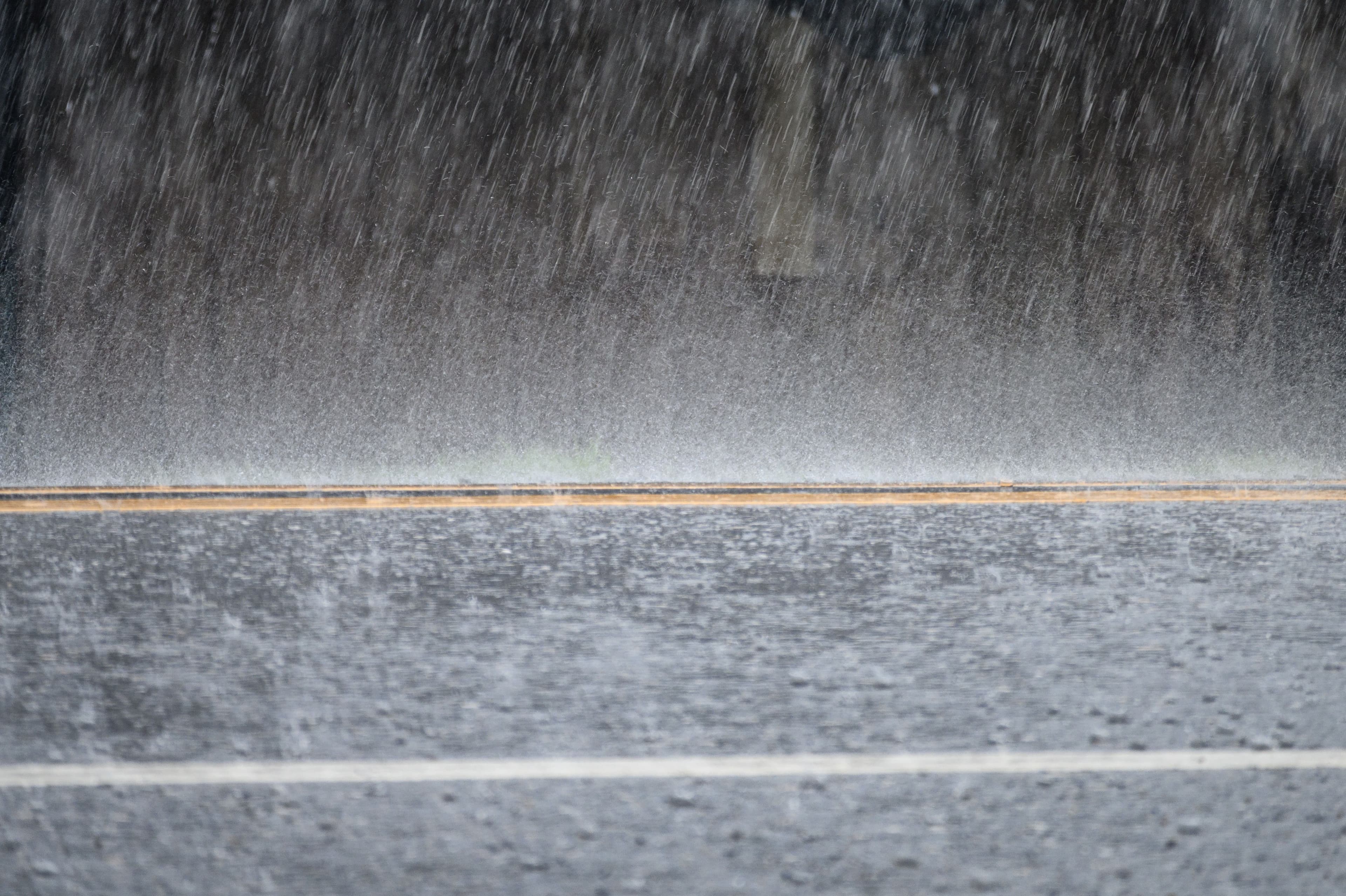 Heavy rain falling on a wet asphalt road with distinct white and yellow lines.